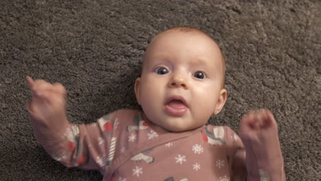 beautiful baby girl lying on soft carpet and watches towards camera, close up top down view