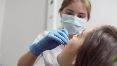 young female dentist in mask approaches with tools. dental lamp lights into a patient's mouth. standing upon a patient