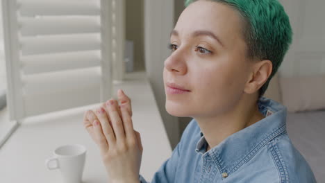 close up of a smiling young woman sitting close to the window in the bedroom while her boyfriend approaching and tenderly hugging her from the back