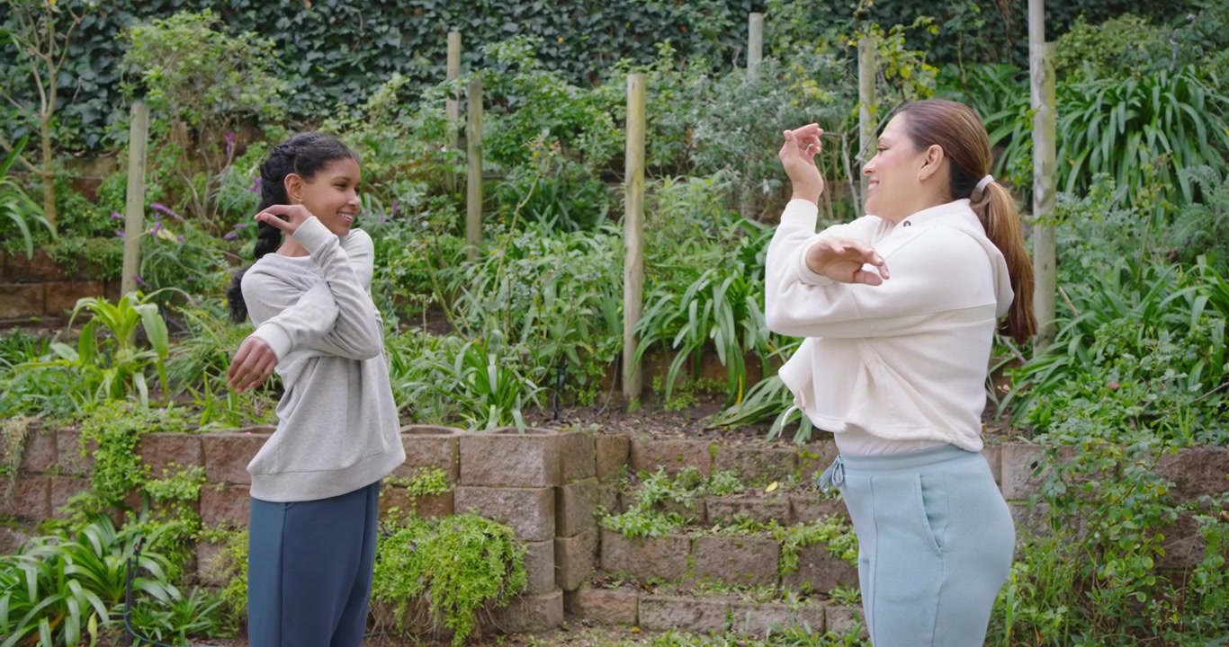 คุณแม่ชาวแอฟริกันอเมริกันกำลังแนะนำลูกสาววัยรุ่นในสวน โดยยกมือขึ้นข้างใบหน้า และลูกสาวทำท่าทางตามพร้อมกุญแจ