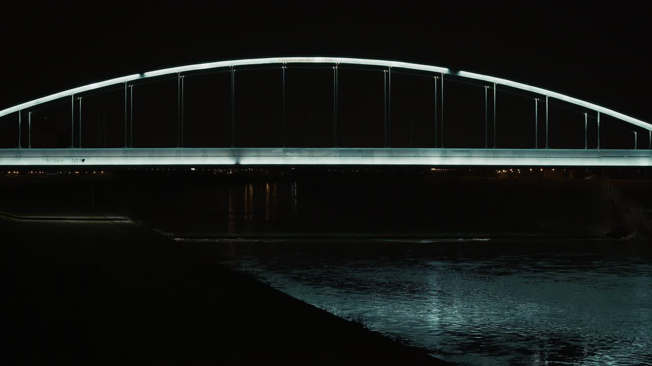 Illuminated railway bridge spans the Sava River reflecting blue light at night
