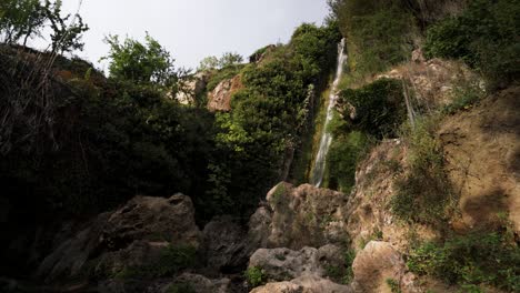 Magical-waterfall-hidden-in-rocky-and-lush-terrain,-zoom-out-view