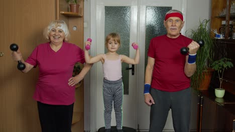 Granddaughter-and-mature-grandparents-in-sportswear-making-sports-jogging-workout-exercises-at-home