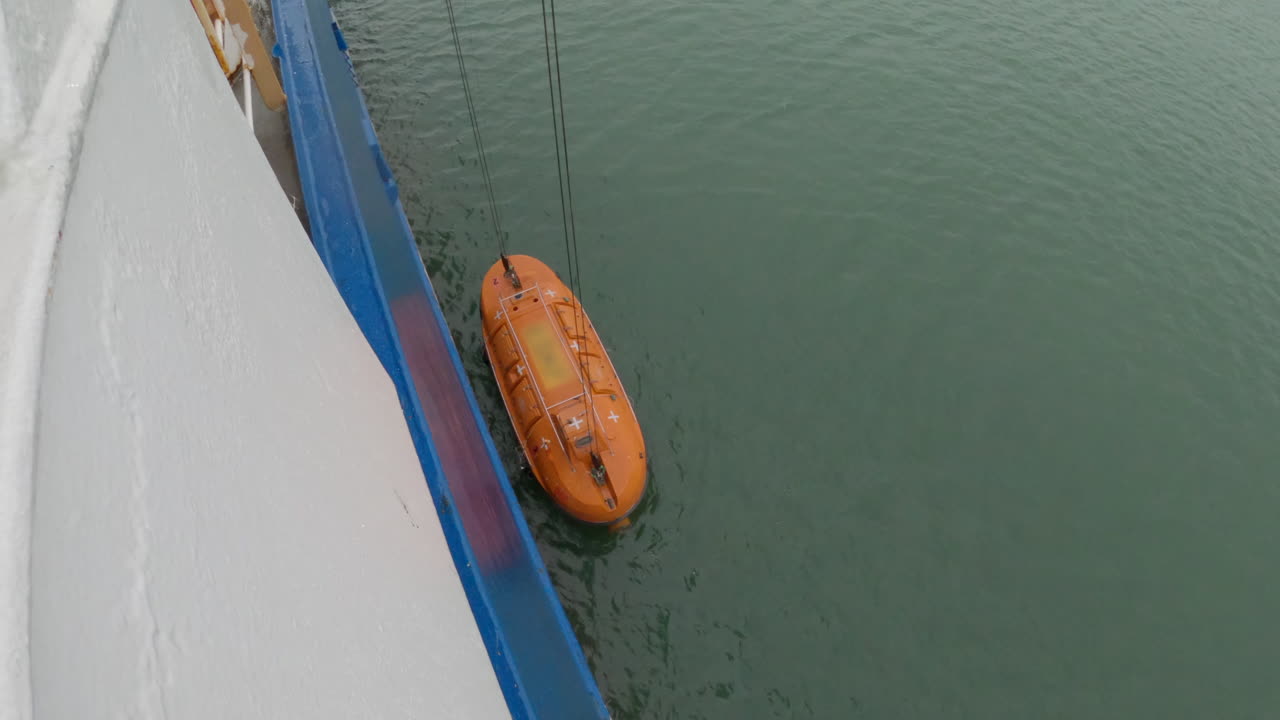 Orange Emergency Lifeboat being released off an industrial ship into the sea, oil and gas industry