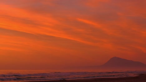 orange dawn skies over beach with rolling waves and mountain in background, panning shot