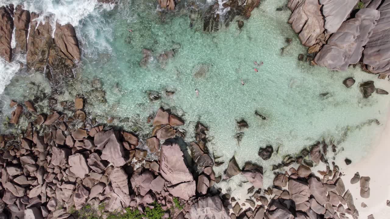 Sahil şeridine yakın granit taşların, berrak turkuaz suyun, şnorkelle yüzen insanların kuş bakışı drone görüntüsü, Anse Cocos, La Digue, Seyşeller 006