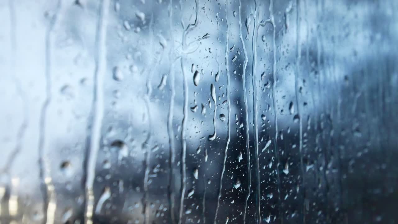 Rainy storm droplets, moody weather fall down window glass closeup bokeh
