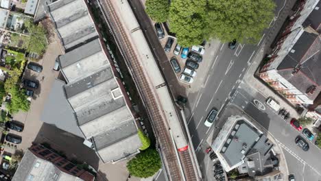 Top-down-drone-shot-of-district-line-train-passing-over-a-road-London