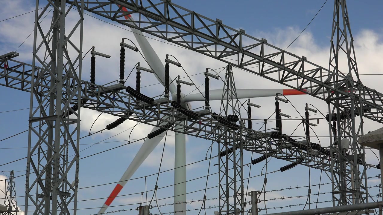 Wind Turbine Rotating Behind Electrical Substation Infrastructure