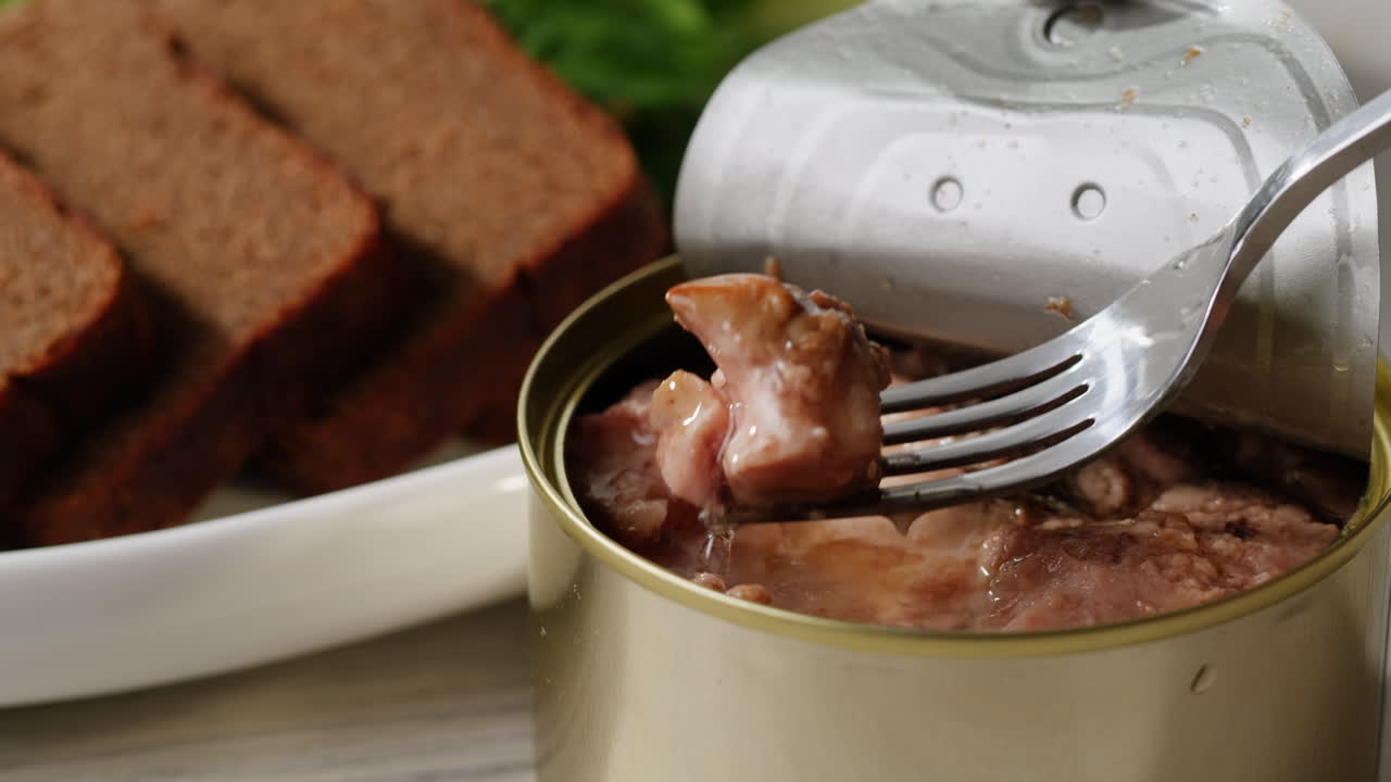 Smoked cod liver in oil in open tin can with fresh greens on wooden table. Seafoods delicacy. High quality 4k footage