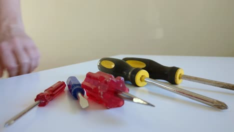 Woman-choosing-screwdriver,-multiple-screwdrivers-on-worktop