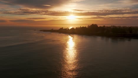 drone shot flying in towards a light house at sunset with hundreds of surfers