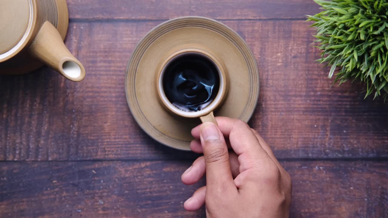 mano sosteniendo una taza de café en una mesa de madera