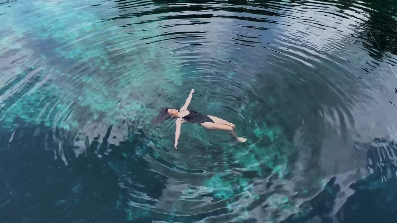 mujer joven flotando en aguas azules claras en cenote corazón en tulum, méxico