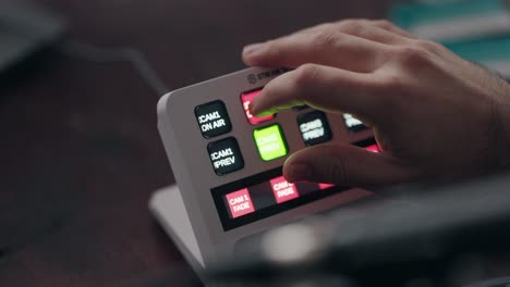 close up of a hand operating a live stream switcher with illuminated buttons for video control