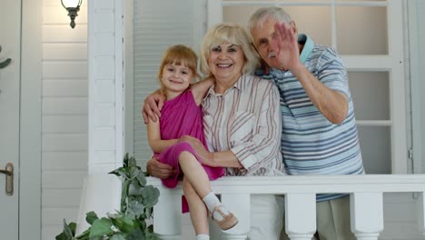 senior grandfather and grandmother couple with granddaughter waving hand, smiling, saying hello