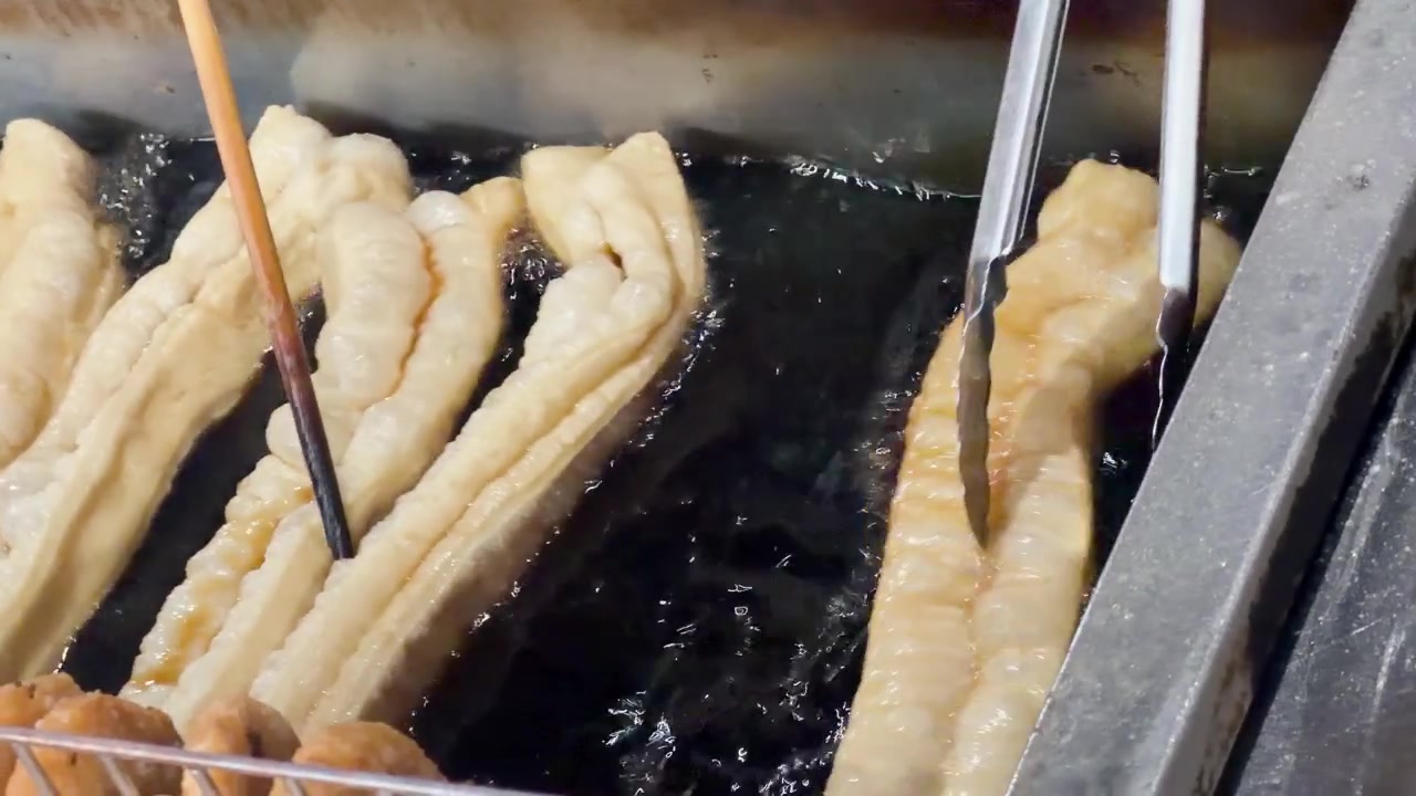 Gros plan de longs bâtonnets de pâte frits dans de l'huile bouillonnante à l'aide de pinces et de baguettes métalliques
