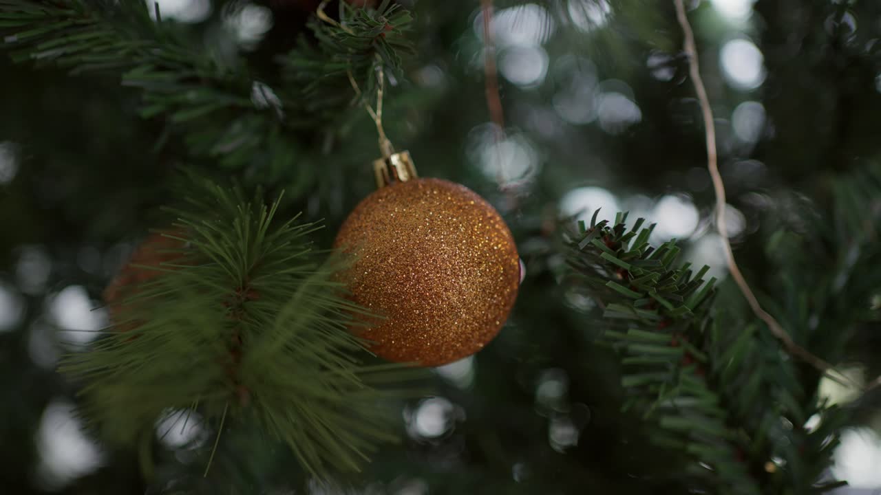 Joulukuusessa roikkuva kultainen glitterikoriste havunoksissa