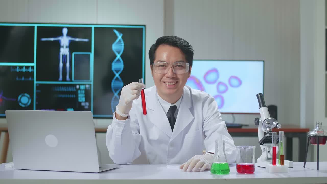 Asian Scientist Researching In The Laboratory With Test Tube, He Warmly Smiles Into The Camera