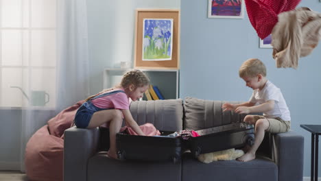 naughty little children throw clothes out of open suitcase