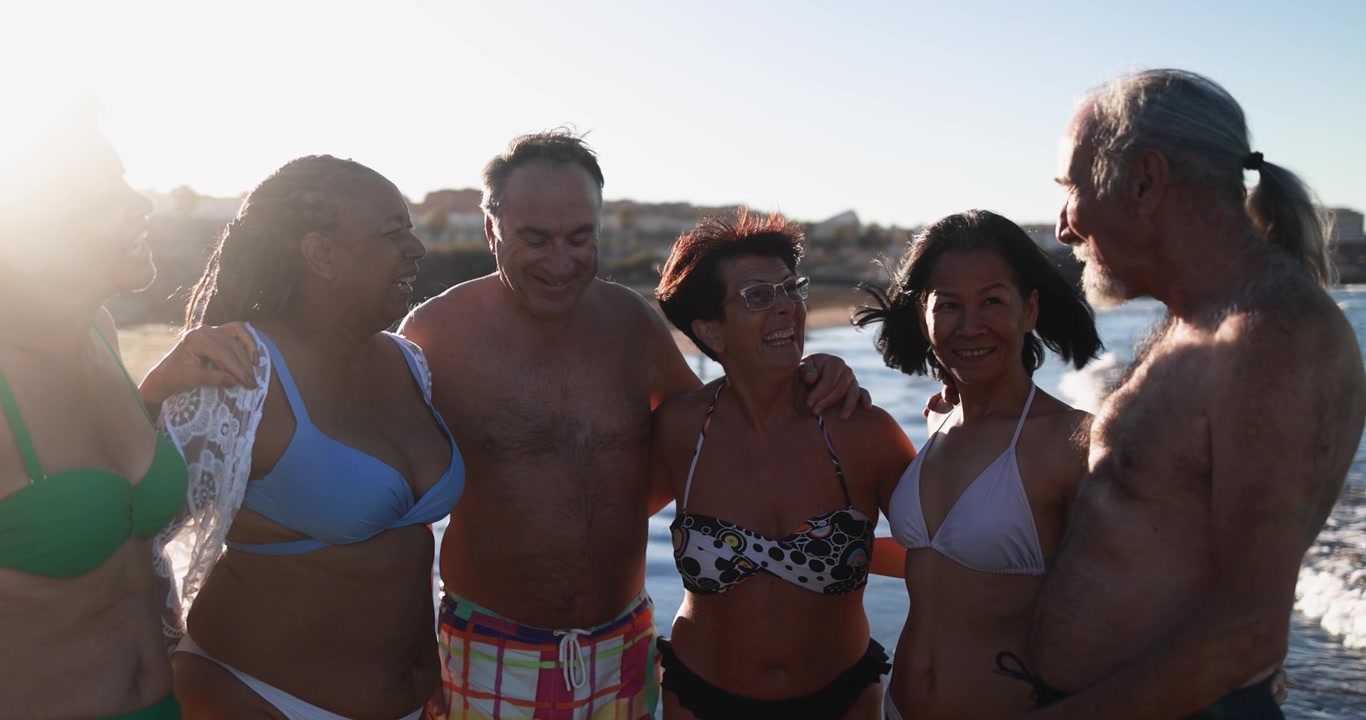 Amigos idosos multiétnicos rindo juntos na praia