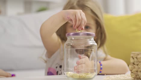 una madre consciente invirtiendo en el futuro lanza oro a su alcancía para su hija.