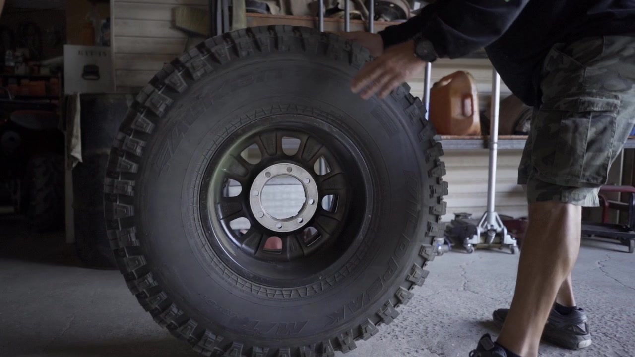 Race car tire being rolled to crew member for race preparation.