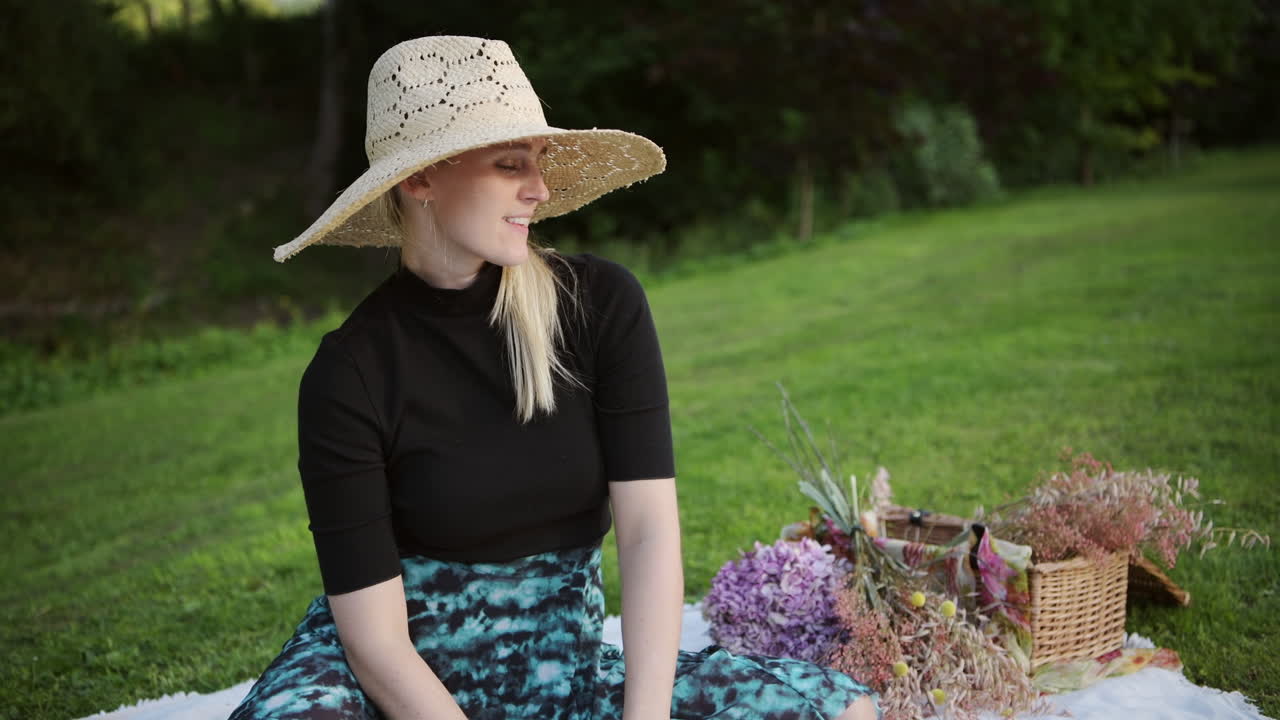 Cute woman with straw hat enjoys picnic in park taking off face mask, end of lockdown concept