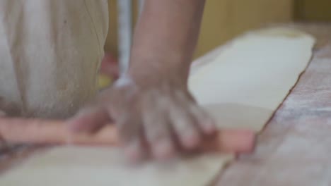 close-up of a pastry chef rolling dough with hands using a wooden rolling pin on a work surface