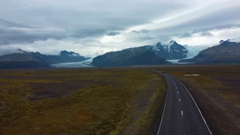 drone following a car going on iceland road towards the snowcapped mountains