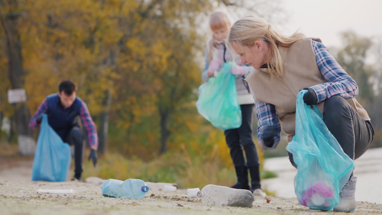 en ung kvinde med børn indsamler skrald langs søen og putter plast i poser