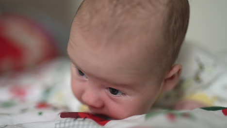 beautiful toddler putting efforts to hold his head up. tiny boy lying on the bed with his head to the camera close up. blurred background.