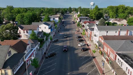 aerial rising shot showing main street of american town with shops at sunrise. summer day in egg harbor, new jersey. water tower in distance. parking cars along road