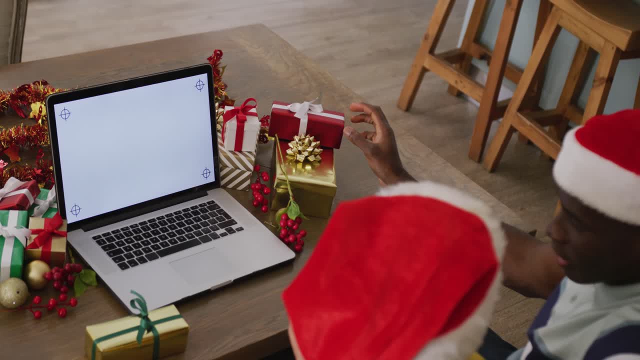 video de una pareja diversa con sombreros de santa haciendo una llamada de video de portátil de navidad, con espacio de copia en la pantalla