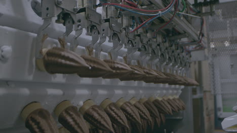 fixed clip showing automated machinery moving rows of chocolate ice cream cones from assembly line to the next step of processing