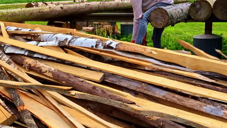 man using chainsaw to cut wooden planks beside timber pile outdoors
