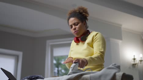 bottom angle view of relaxed happy african american housewife dancing to music ironing laundry at home. portrait of cheerful young woman having fun housekeeping indoors.