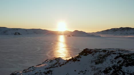 frozen lake with sunset, sunrays reflecting on ice, and people