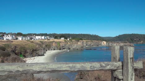 Beautiful-dolly-shot--wooden-fence-frames-a-blue-sky-day-view-of-a-small-beach-and-historic-buildings-Mendicino-CA-3