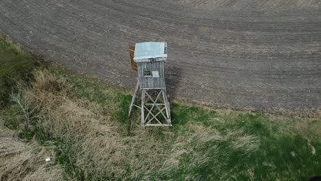 Hunting-pulpit-in-the-outdoors,-high-seat-shooting-pulpit-in-a-field,-aerial-orbital-shot-of-a-hunters-observation-point