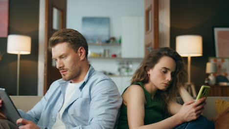 Closeup-serious-duet-sitting-home.-Couple-reading-devices-ignoring-each-other