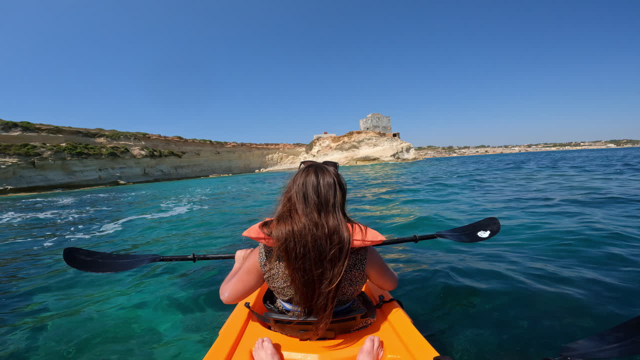 una mujer en un kayak naranja remando hacia la costa rocosa de malta