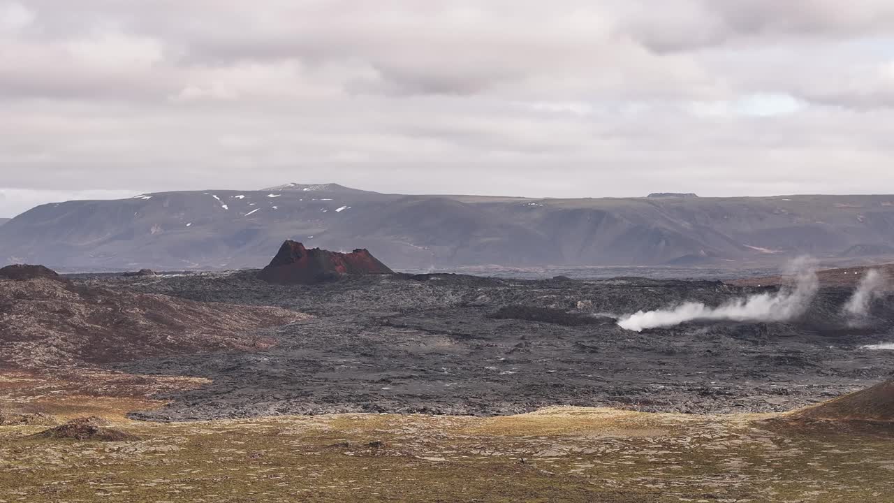 Volcanic landscape in Iceland showing dark lava fields and geothermal steam rising from the ground.