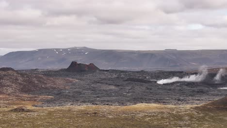 volcanic landscape in iceland showing dark lava fields and geothermal steam rising from the ground.