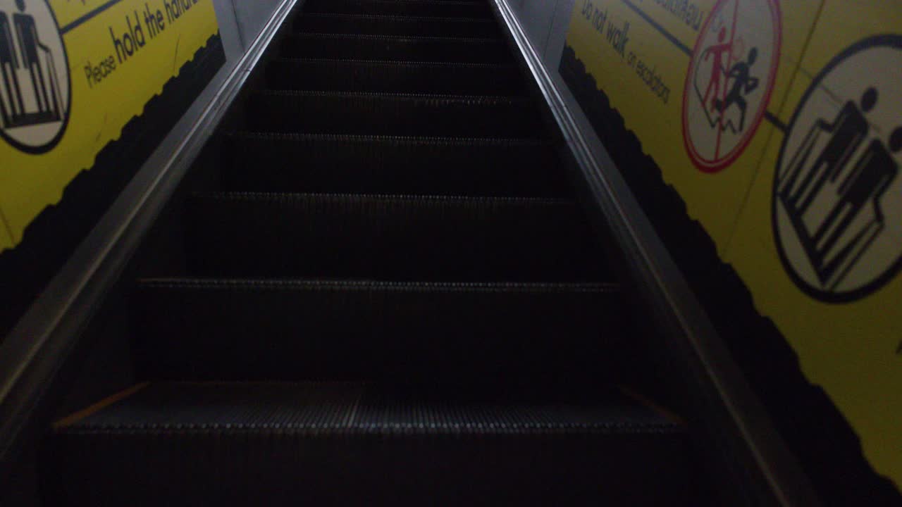 First-person perspective moving up a metallic escalator from a dark tunnel into bright daylight