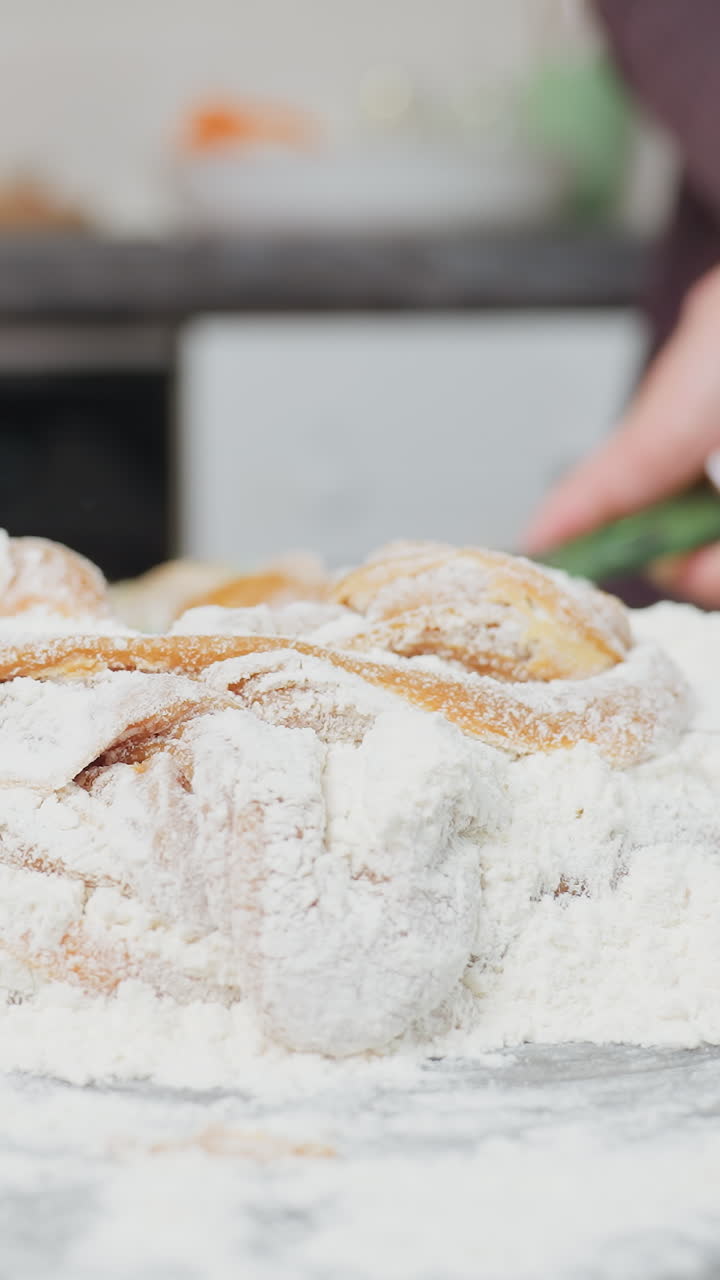Close-up of person in maroon cloth kneading and mixing dough with flour on kitchen countertop, hands actively blending ingredients, dusted with flour, as soft dough takes shape for baking