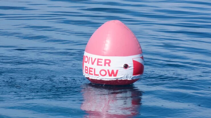 Red and white dive buoy marker safety equipment floating on surface of ocean with bubbles from scuba divers below