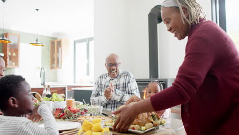 happy african american multi generation family serving food at thanksgiving dinner, slow motion