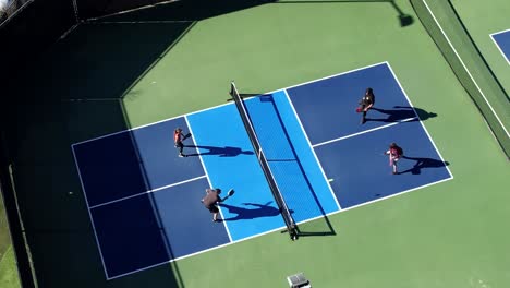 pickleball foursome playing on sunny day hitting ball over net, aerial descending down over court