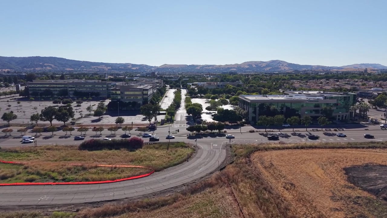 Riprese aeree con drone catturano i parchi uffici di Dublino, California, strade tortuose, parcheggi illuminati dal sole, praterie secche, cielo azzurro limpido e colline panoramiche in una composizione orizzontale nitida.